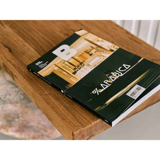 Magazine B - Issue 92 % Arabica The magazine is displayed on a wooden shelf, emphasizing its stylish cover featuring a % Arabica coffee bar and complementing the brand’s minimalist design ethos.