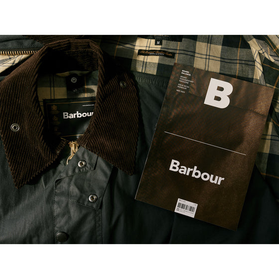 Magazine B - Issue 94 Barbour The magazine is displayed next to a Barbour jacket, highlighting the connection between the publication and the brand’s renowned waxed cotton outerwear.