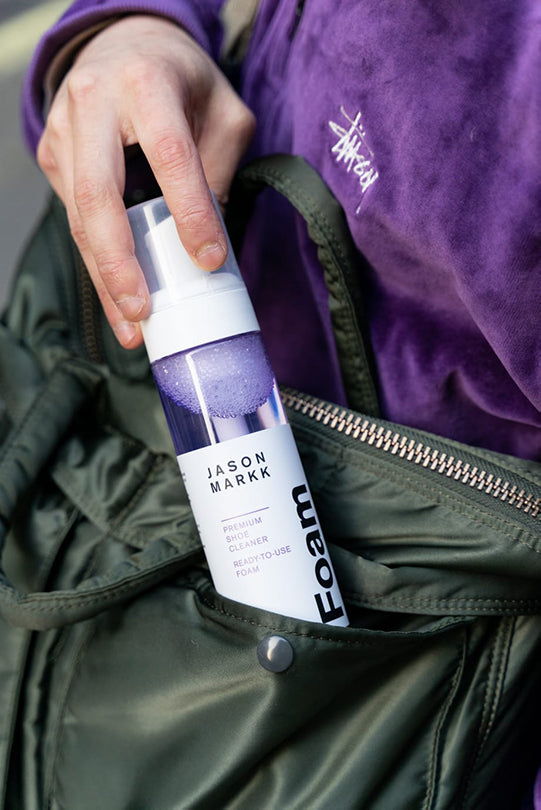 Jason Markk RTU Foam Shoe Cleaner. A person placing the foam cleaner into a bag, highlighting its portability and ease of use on-the-go.